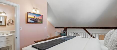 A bedroom with a bed, a nightstand, a dresser, a painting, and a sloped ceiling.