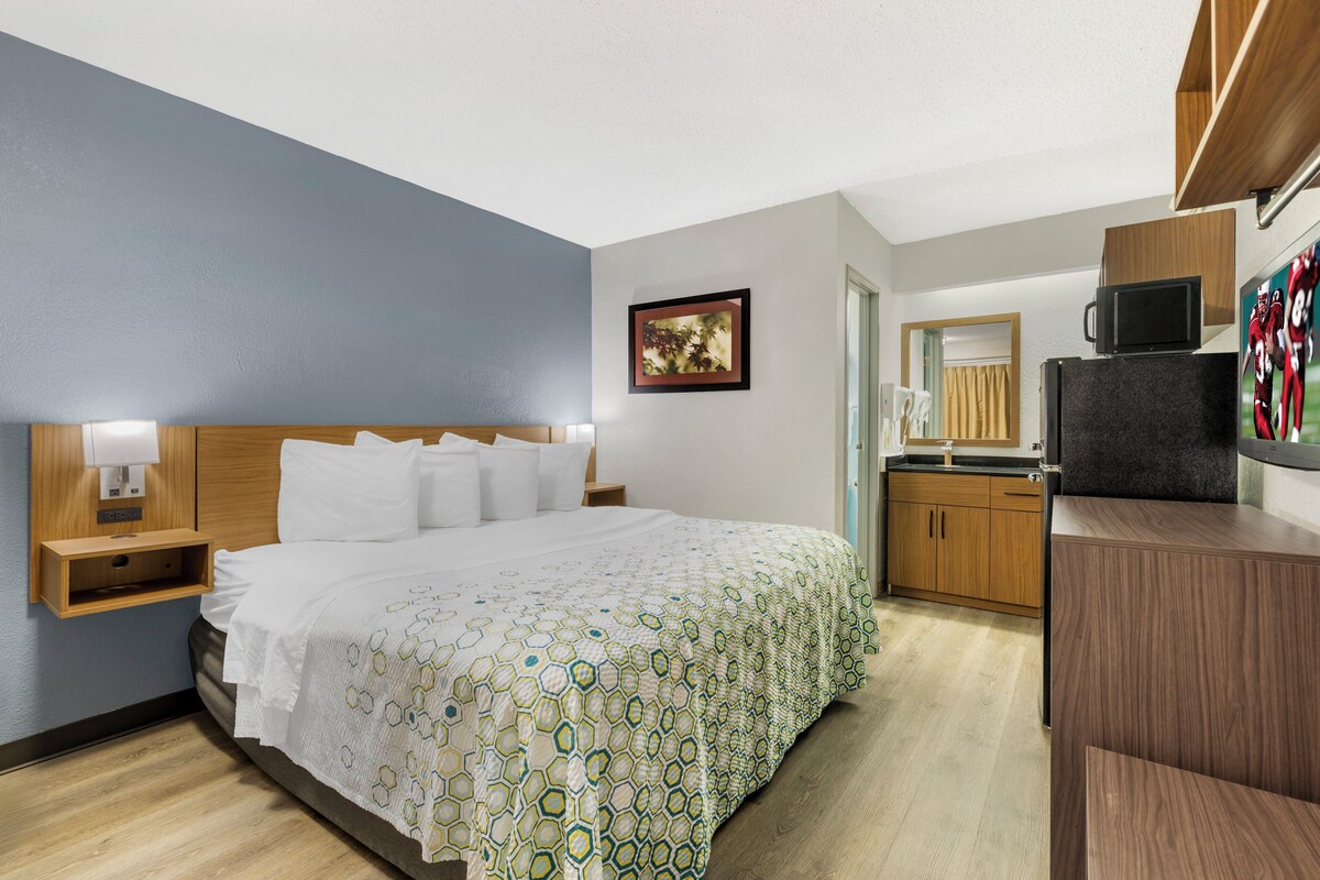 Ein Hotelzimmer mit einem großen Bett, einem Holz-Kopfteil, einem Nachttisch mit Lampe, einem kleinen Holzschrank, einer Mikrowelle und einer Holzausstattung mit Spüle.