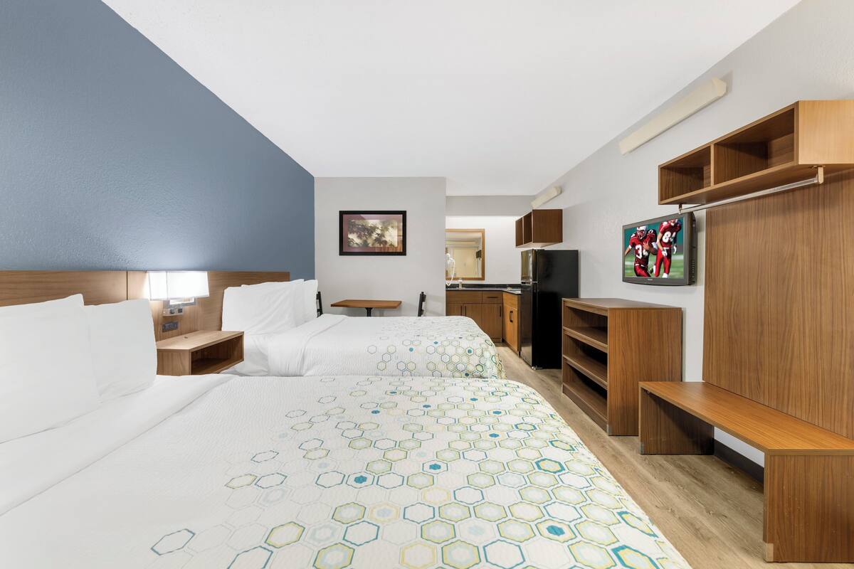 A hotel room with two beds, a TV, wooden furniture, and a painting on the wall.
