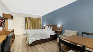 Ein Hotelzimmer mit Bett, Schreibtisch, Stuhl, Tisch und Fernseher.