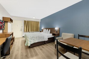 Ein Hotelzimmer mit Bett, Schreibtisch, Stuhl, Tisch und Fernseher.