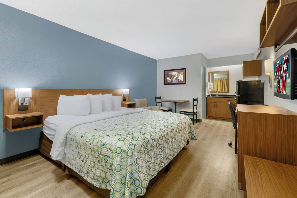 A hotel room with a large bed, a desk, a chair, a television, and a mirror.