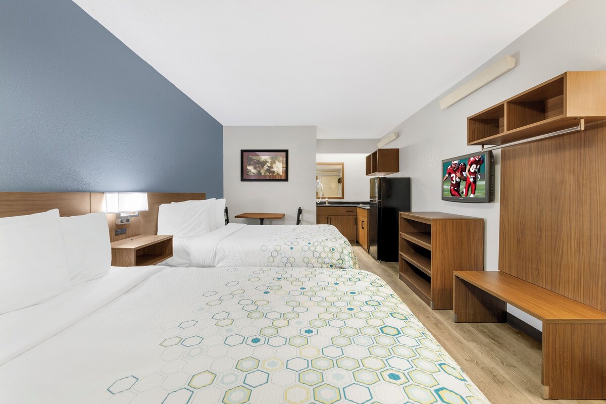 Une chambre d’hôtel avec deux lits, une télévision, des meubles en bois et un tableau au mur.