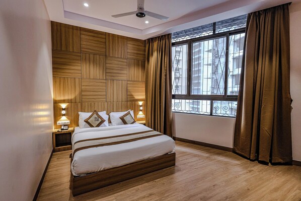 A hotel room with a large bed, wooden headboard, bedside lamps, and a window with curtains.