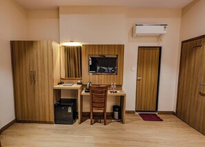 A compact hotel room with a wooden desk, a chair, a television, a wardrobe, and an air conditioning unit. - Hotel Alfa Suites (Mumbai)