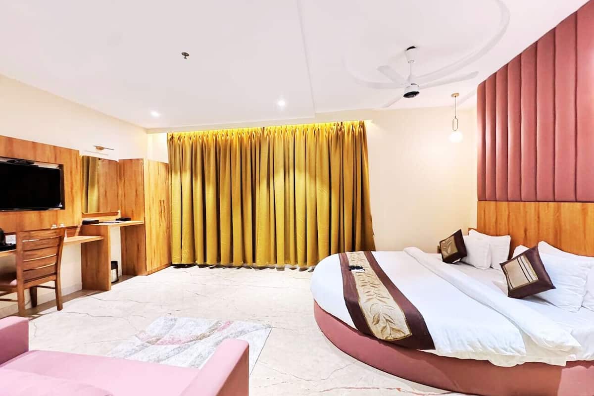A modern hotel room with a large bed, a desk, a TV, and a window with curtains.