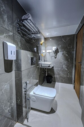 A modern bathroom with a built-in sink, a toilet, a towel rack, a soap dispenser, and a handheld showerhead. - Hotel Alfa Suites (Mumbai)