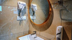 Un bagno moderno con una parete in marmo, uno specchio rotondo, un lavabo bianco e due asciugacapelli fissati alla parete.