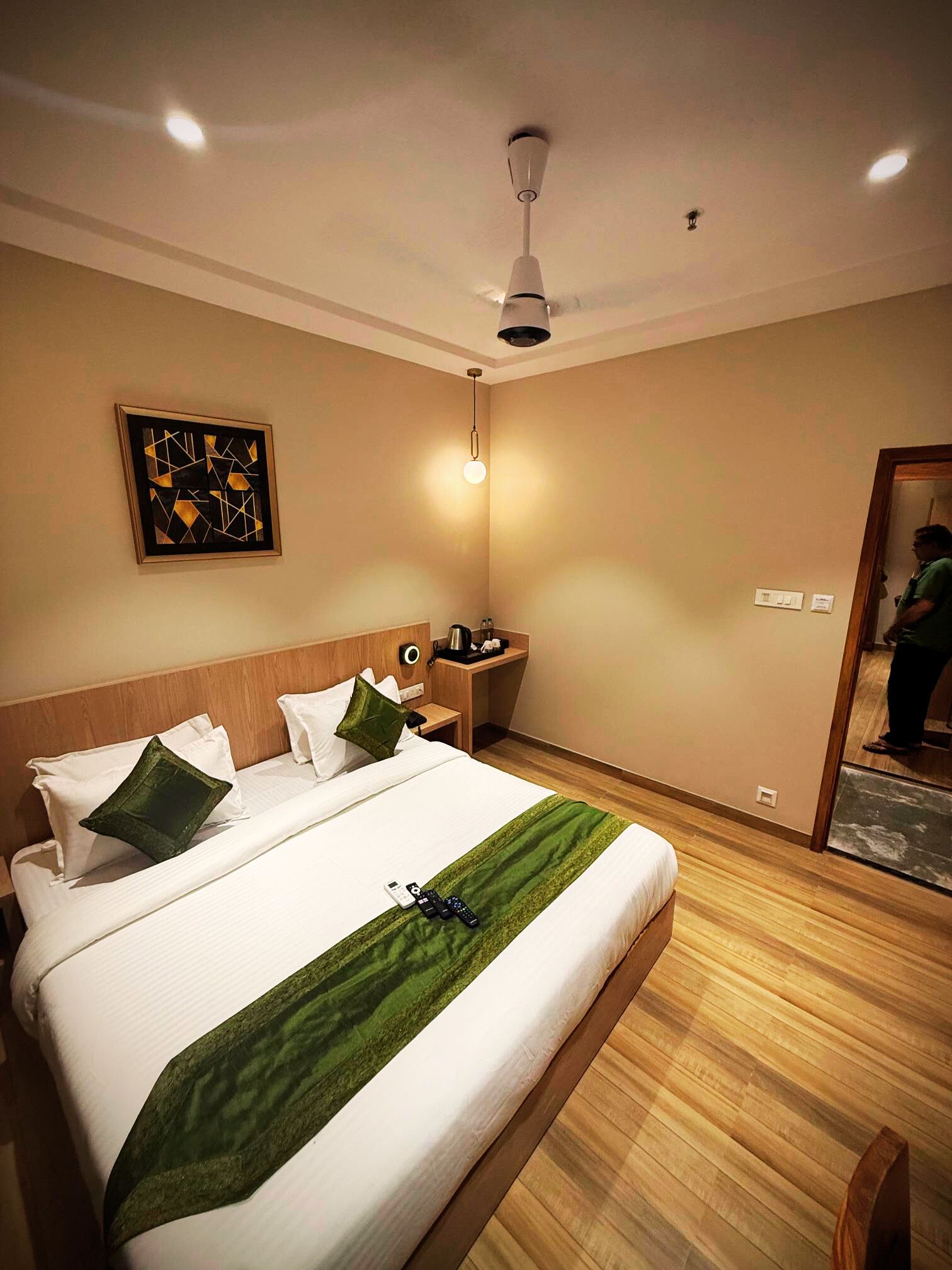 Habitación de hotel con una cama grande, una mesita de noche con lámpara, un cuadro en la pared y un espejo en la esquina.