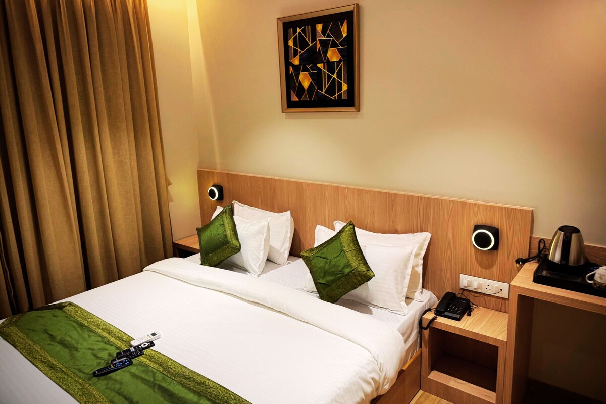 A hotel room with a bed, a nightstand, a coffee maker, and a wall-mounted artwork.