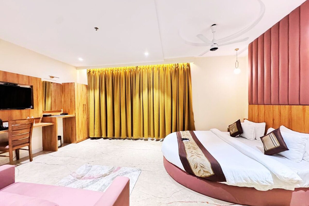 Ein modernes Hotelzimmer mit einem großen Bett, einem Schreibtisch, einem Fernseher und einem Fenster mit Vorhängen.