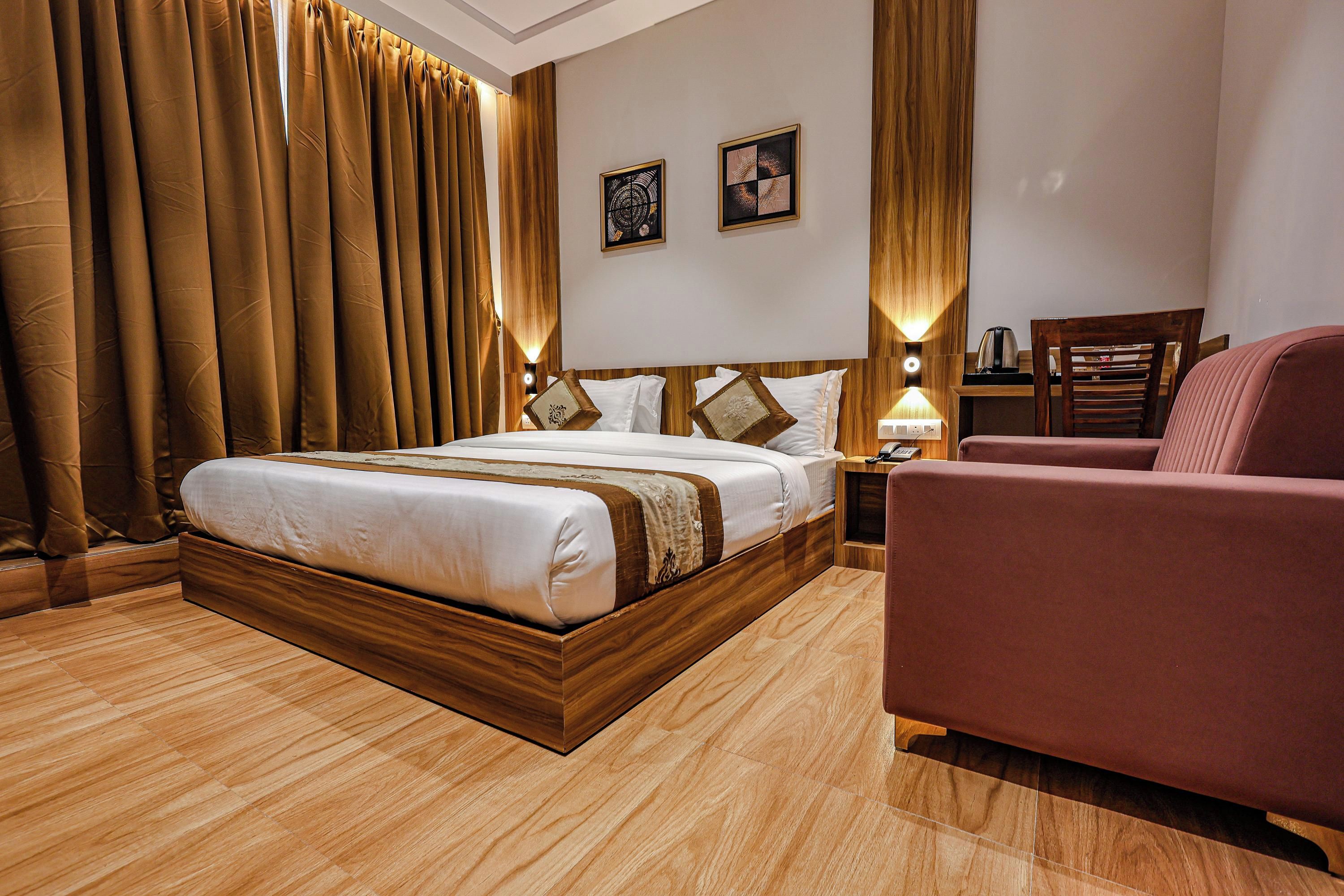 Une chambre d’hôtel avec un grand lit, une tête de lit en bois, deux tables de chevet avec des lampes, une petite table de nuit en bois, un fauteuil rouge et un plancher en bois.