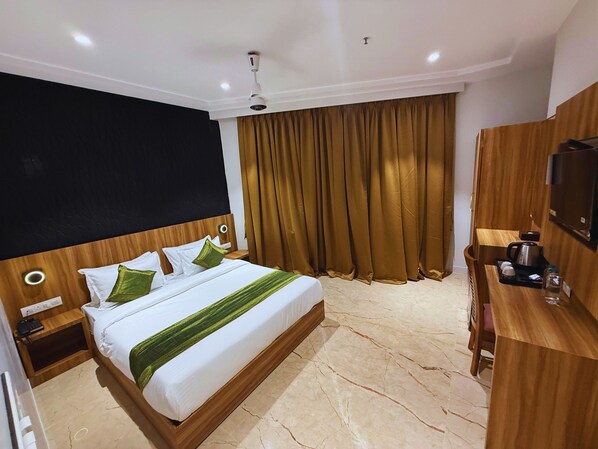 Ein Hotelzimmer mit einem Bett, einem hölzernen Kopfteil, Vorhängen, einem Fernseher und einer Kaffeemaschine.