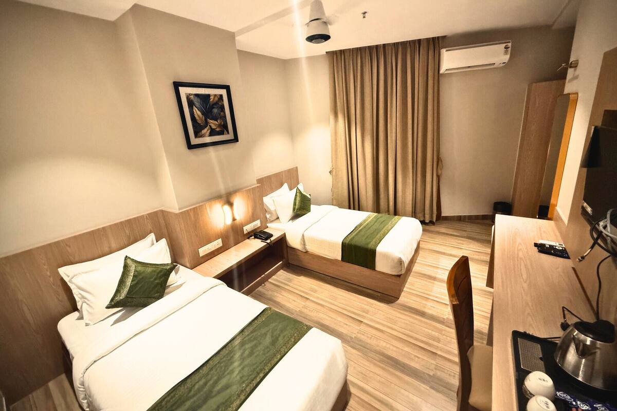 A hotel room with two beds, a desk, a chair, a TV, and an air conditioning unit.