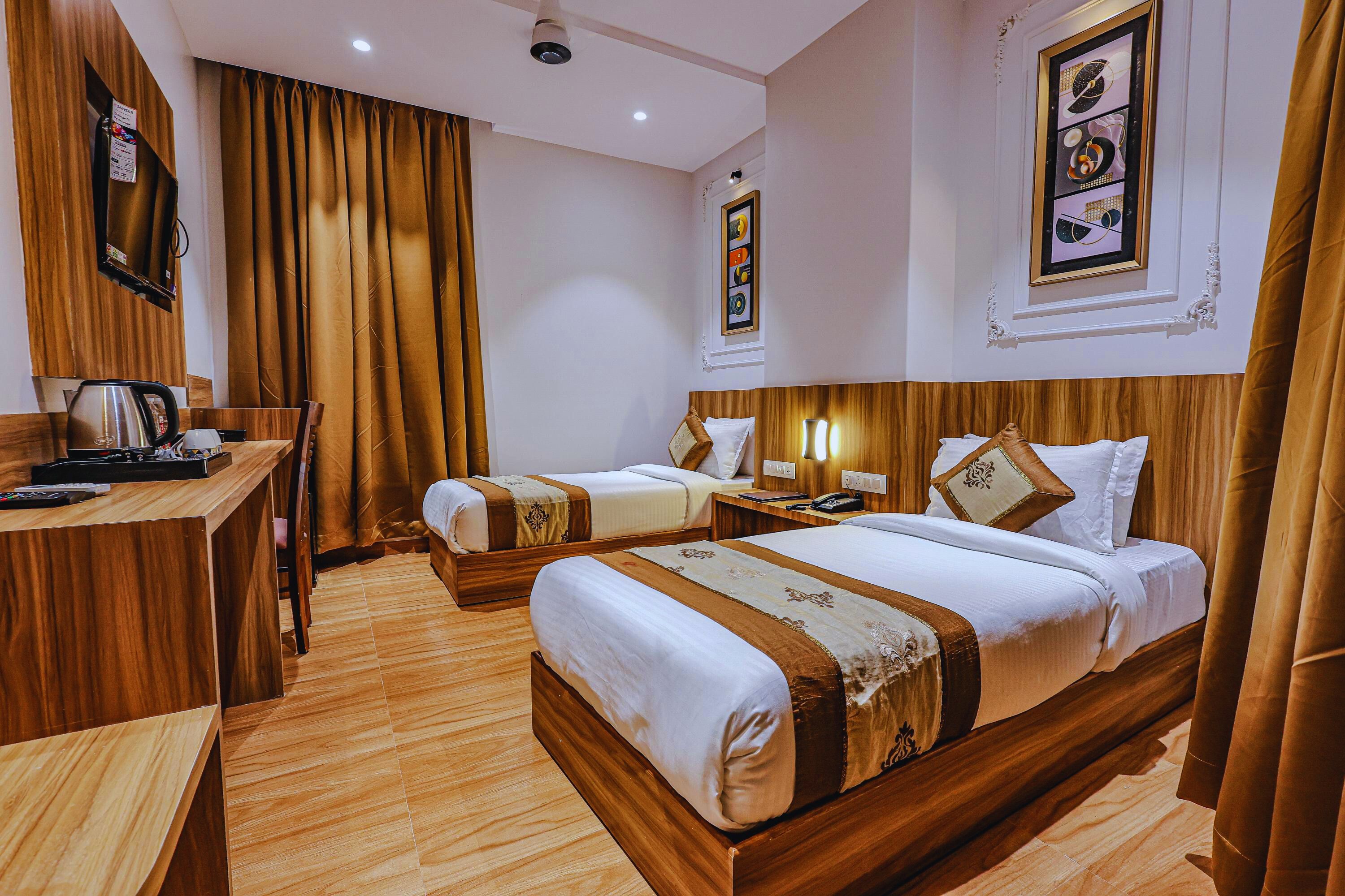 A hotel room with two beds, a wooden desk with a kettle, and a framed picture on the wall.
