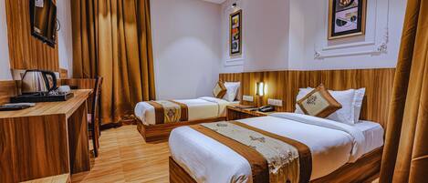 A hotel room with two beds, a wooden desk with a kettle, and a framed picture on the wall.