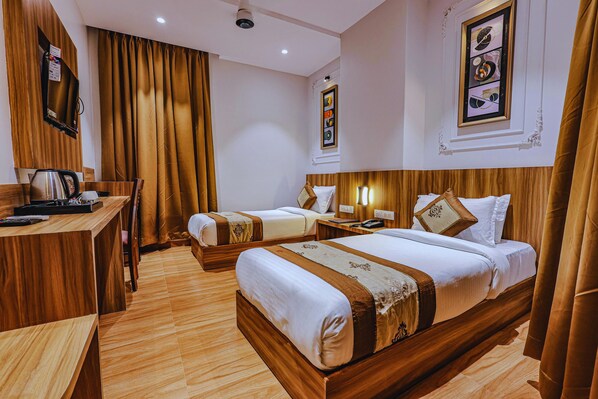 A hotel room with two beds, a wooden desk with a kettle, and a framed picture on the wall. - Hotel Alfa Suites (Mumbai)