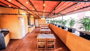 An indoor patio area with wooden tables and chairs, potted plants, and a red ceiling. - Hotel Alfa Suites (Mumbai)