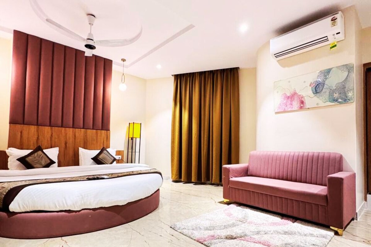 A modern bedroom with a curved bed, a pink sofa, a marble floor, and a ceiling fan.