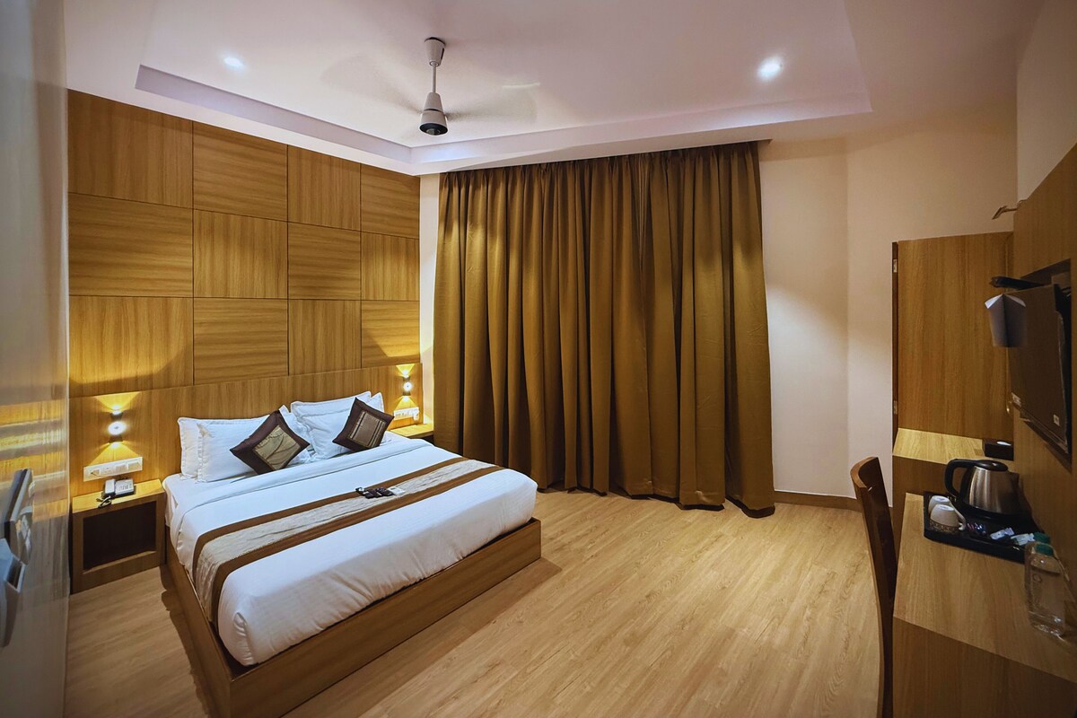 A modern hotel room with a wooden headboard, a large bed with white bedding, a ceiling fan, and a wooden desk with a kettle and cups.