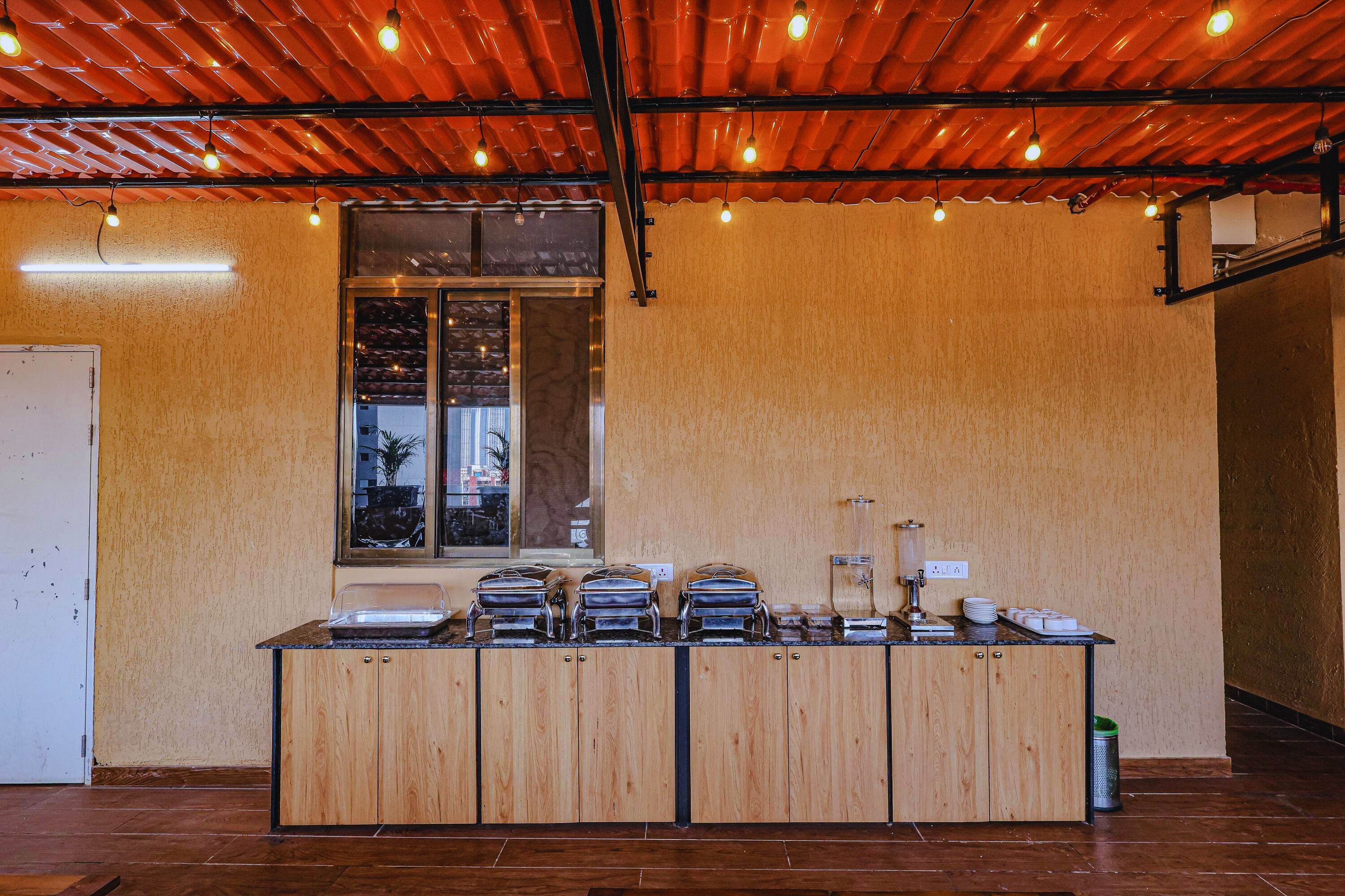 A buffet setup with multiple serving stations, a window with a view, and a ceiling with exposed beams and lighting.