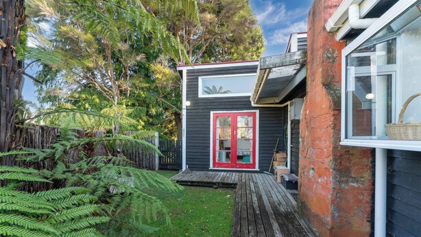 A small house with a red door, a wooden deck, and a garden with ferns. - Singlee - Turangi Holiday Home (Turangi)