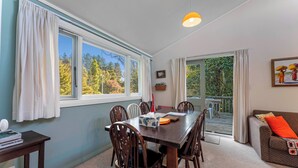 A dining area with a wooden table, chairs, and a view of the outdoors through large windows. - Singlee - Turangi Holiday Home (Turangi)