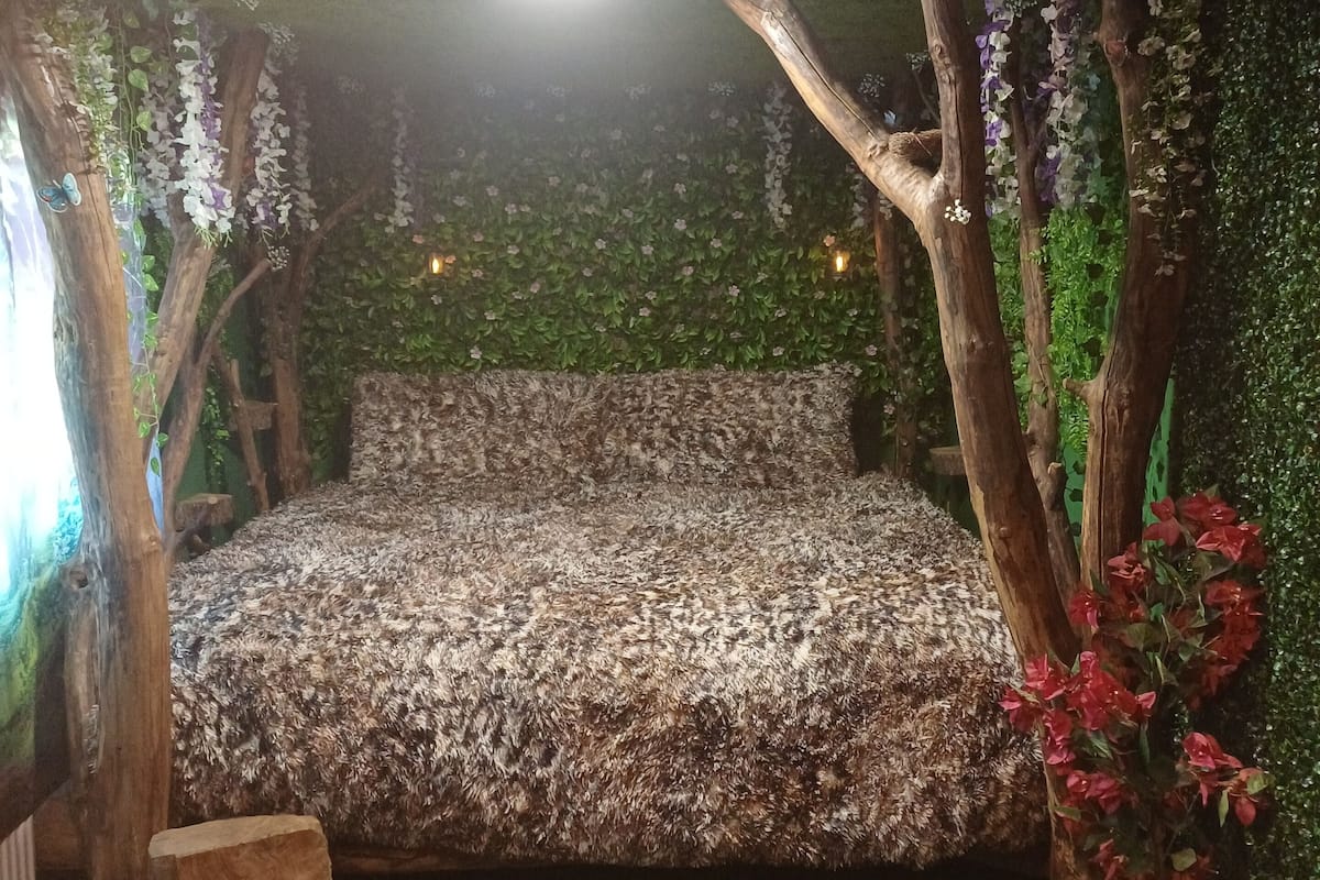 A room with a bed, artificial trees, and a wall with green foliage.