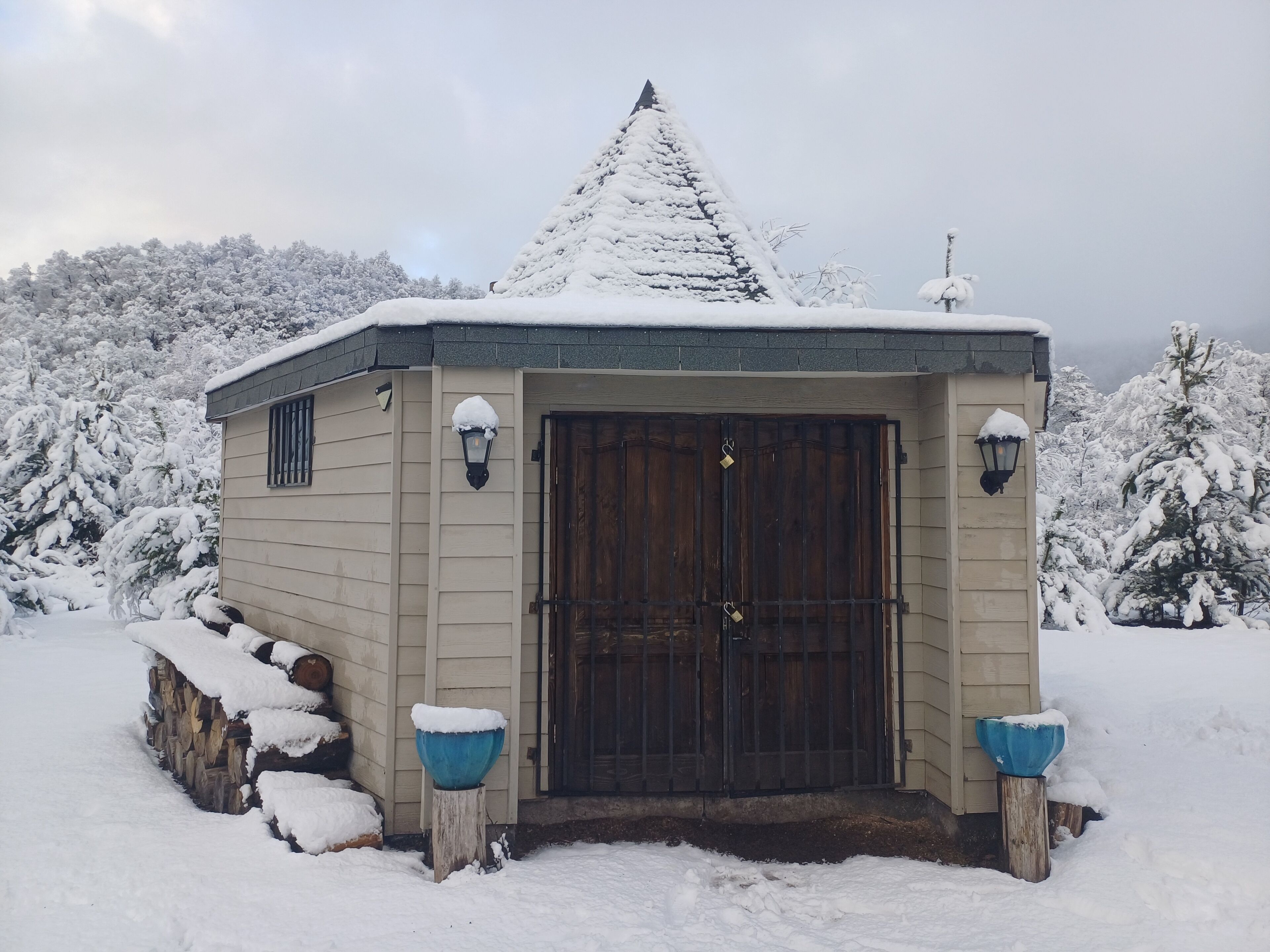Een klein, met sneeuw bedekt gebouw met een donkere houten deur, twee wandlampen en een besneeuwd dak.