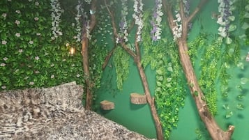 A room with a green wall, wooden tree branches, hanging plants, and a patterned rug.