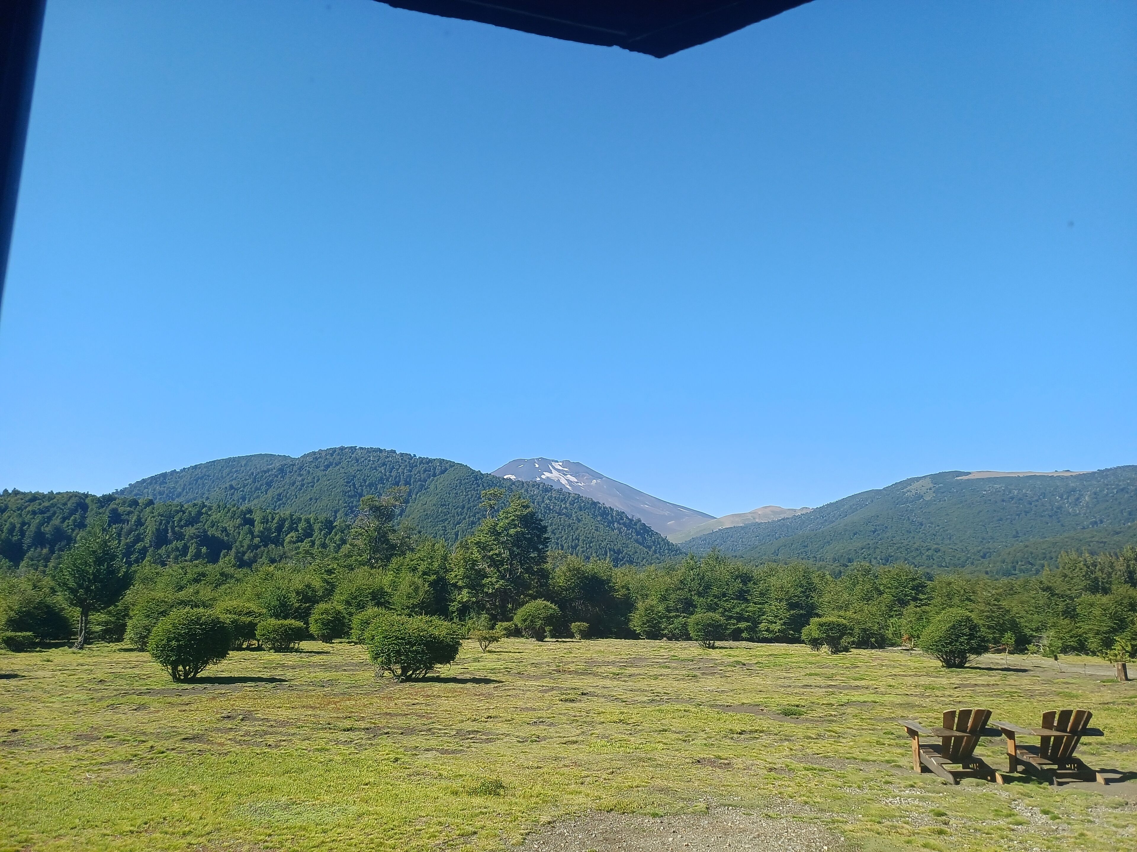 A view of a mountain range with a clear sky. There are two wooden chairs in the foreground.