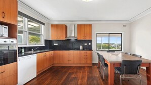 A modern kitchen with wooden cabinets, a black backsplash, and a dining area with a table and chairs.