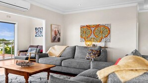 A living room with a grey sofa, a wooden coffee table, and a large window offering a view of the outdoors.