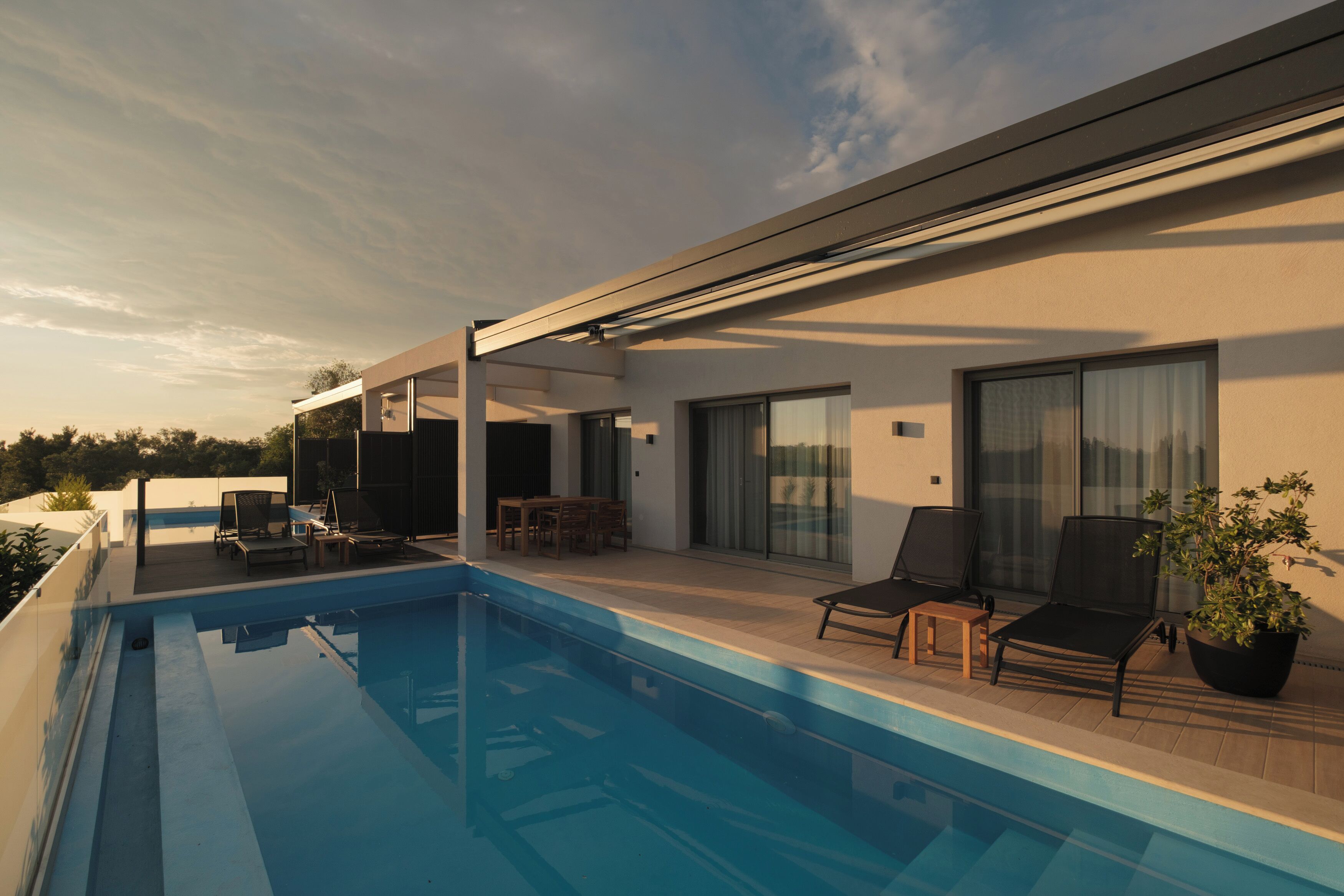 Zona de piscina exterior moderna amb gandules i una taula, envoltada per un porxo cobert.