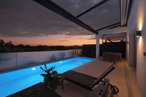 A modern outdoor pool area with a view of the sunset, a covered seating area, and a well-lit pathway. - VILA 2 ANAPNOE IKIES CORFU WITH PRIVATE POOL (Corfu)