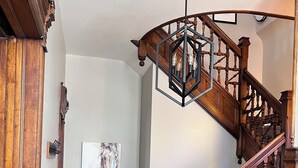 A wooden staircase with a geometric light fixture, a framed artwork on the wall, and a wooden door. - The Tower on Summit (Eau Claire)