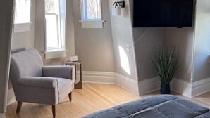A bedroom with a large bed, a chair, a small table, a potted plant, and a TV mounted on the wall. - The Tower on Summit (Eau Claire)