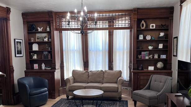 A living room with a beige sofa, two armchairs, a coffee table, and a bookshelf. - The Tower on Summit (Eau Claire)