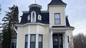 A two-story Victorian-style house with a black roof, white trim, and a prominent bay window. - The Tower on Summit (Eau Claire)