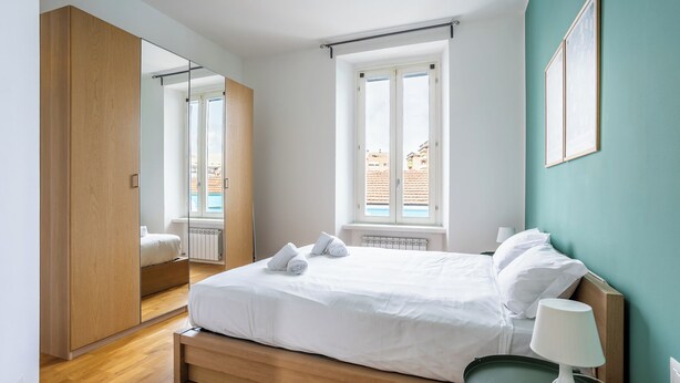 Une chambre avec un grand lit, une table de chevet avec une lampe, un miroir et une vue sur une piscine par la fenêtre.