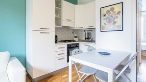 Une cuisine de taille réduite avec des meubles blancs, une cuisinière à gaz et une table à manger avec des chaises.