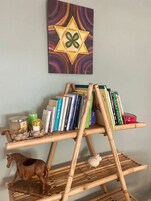 Una estantería de madera con libros y objetos decorativos, una escultura de caballo de madera y una pared con un cuadro de motivos geométricos.