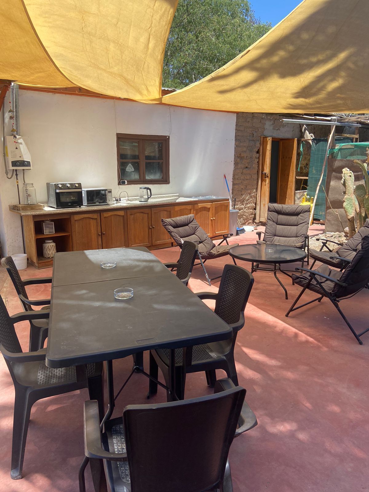 Un patio al aire libre con una mesa y sillas, una pequeña cocina con microondas y una ventana.