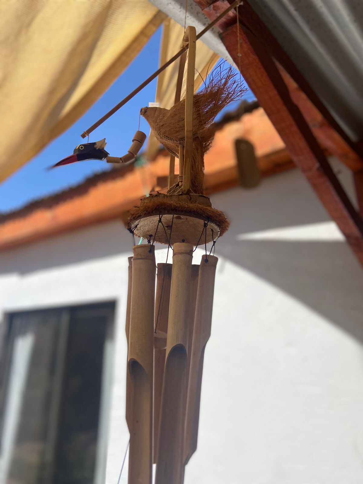 Un carillon éolien composé de tubes en bambou et d’une figurine d’oiseau, suspendu à l’extérieur.
