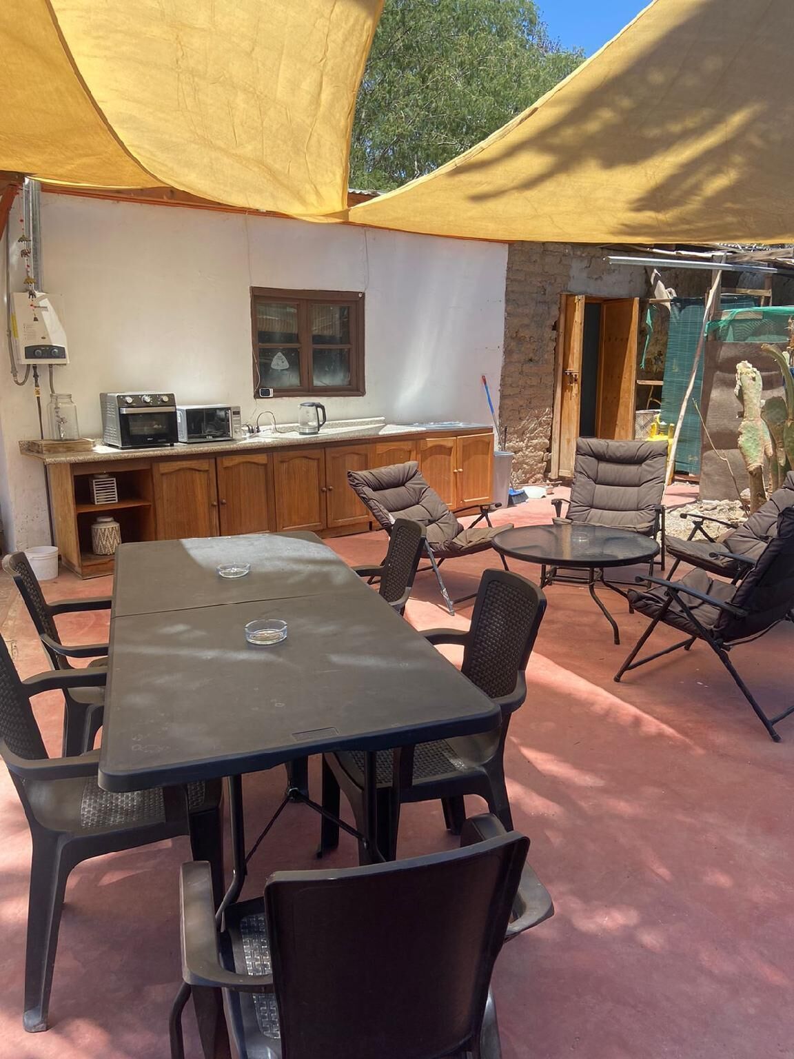 Un área de cocina al aire libre con una mesa, sillas, microondas y cafetera.
