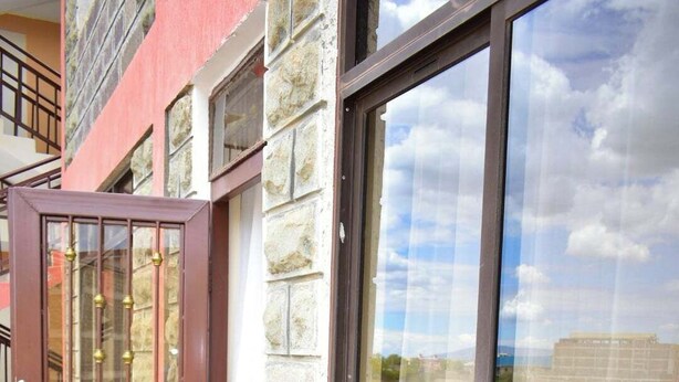 A balcony with a wooden floor, a glass door with a metal gate, and a large window with a view of a building. - The Urban Cabin Naivasha (Naivasha)