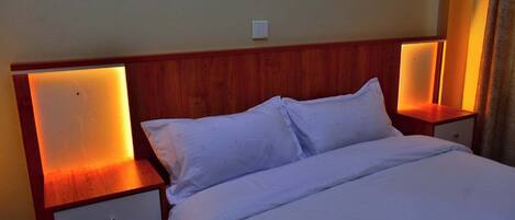 Una habitación de hotel con cabecera de madera, ropa de cama blanca y lámparas de noche.