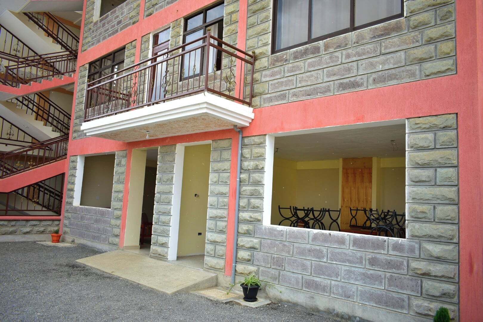 Un edificio de varios pisos con fachada roja y gris, una escalera central y un balcón con barandillas de metal.