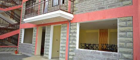 Un edificio de varios pisos con fachada roja y gris, una escalera central y un balcón con barandillas de metal.
