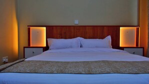 A neatly made bed with white linens and a patterned throw blanket, flanked by two bedside tables with illuminated lamps, in a room with wooden paneling and a neutral wall color. - The Urban Cabin Naivasha (Naivasha)